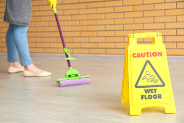 Caution sign and female janitor mopping floor in room, closeup