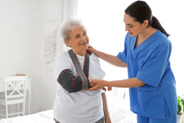 Obraz premium Physical therapist and senior woman with bandaged arm in bedroom