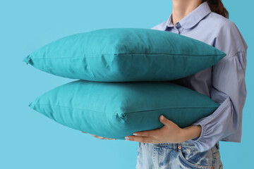 Woman with soft pillows on blue background, closeup