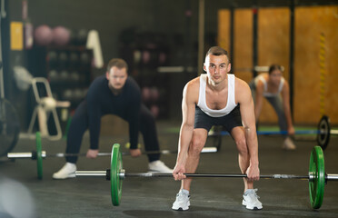 Strong young man practicing with barbell in exercise room during weight training classes