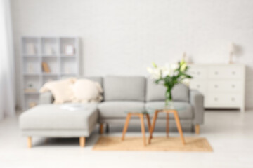 Interior of stylish living room with grey sofa, pillows and vase of lily flowers on coffee table, blurred view