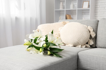 Interior of stylish living room with bouquet of lily flowers on grey sofa, pillows and shelving unit