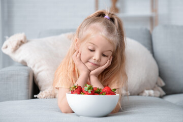 Little girl with bowl of tasty strawberries in living room