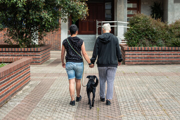 Short-haired gay woman couple holding hands walking in the park with their dog