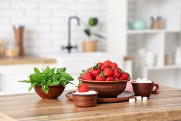 Bowls with tasty strawberries, sugar and mint on table in kitchen