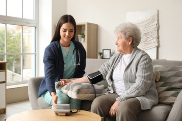 Young caregiver measuring blood pressure of senior woman at home