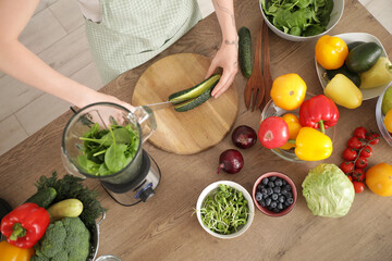 Young woman cutting cucumber for smoothie in kitchen, top view