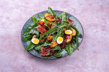 Traditioneller Südtiroler Löwenzahnsalat mit Frühstücksspeck, Bratkartoffel und Wachteleier serviert als Nahaufnahme auf einem Nordic Design Teller