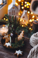 Xmas spirit, simple way to creating holiday atmosphere and festive mood at home on the window sill. Scented burning aromatic candles on wooden tray, liquid reed diffuser with sticks, fir tree branch