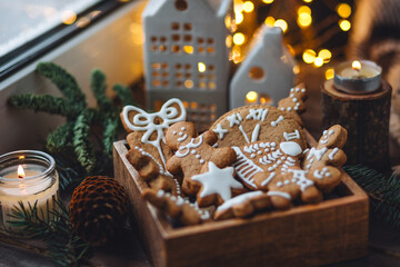 Concept of home christmas or new year celebration, family traditions. Assortment of gingerbread cookies with icing in a vintage wooden box on a window sill with atmospheric lights