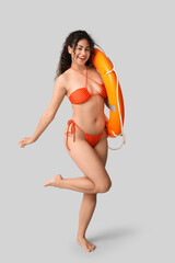 Beautiful young African-American woman in stylish orange swimsuit with lifebuoy on grey background