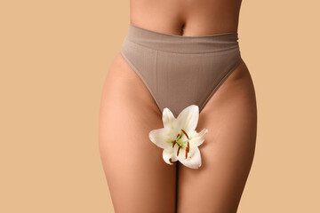 Beautiful young African-American woman in panties with white lily flower on beige background,...