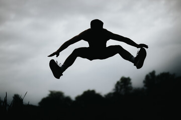 Silhouette of a man performing high jumps in an outdoor setting under a dramatic cloudy sky.