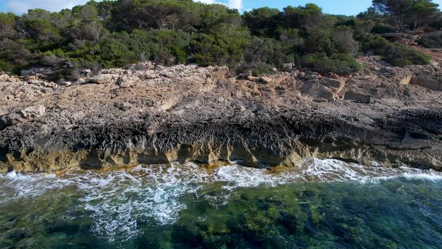 4K Aerial Drone video of the rocky coast with crystal clear water in Mallorca with rough waves crashing against the cliffs on a sunny summer day