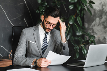 Frustrated young businessman solving difficult task at work place using laptop. Manager CEO doing...
