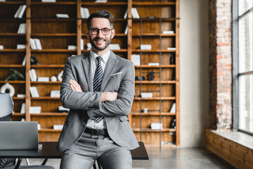 Portrait of young rich businessman in formal suit with arms crossed looking at the camera in modern office. Wealthy foreman manager working, making money at workplace
