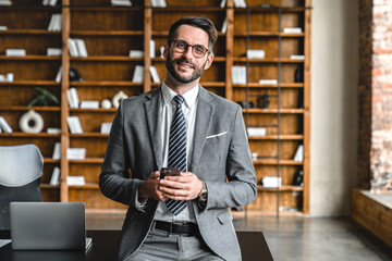 Pensive young businessman using cellphone while working at modern workplace office. Foreman manager boss lawyer checking news, social media, ordering delivery on smart phone remotely
