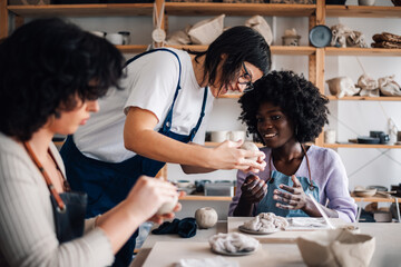 Diverse pottery class attendees learning clay work with tutor at studio