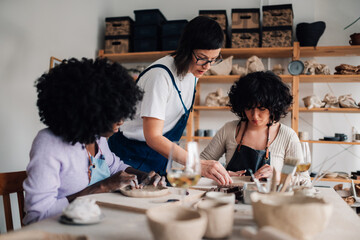 Diverse pottery course attendees sitting and learning pottery with tutor