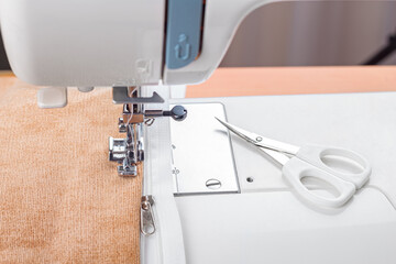 Modern sewing machine special presser foot with beige corduroy fabric and thread, closeup. Sewing process of sewing on a zipper. Business, hobby, handmade, zero waste, recycling, repair concept.