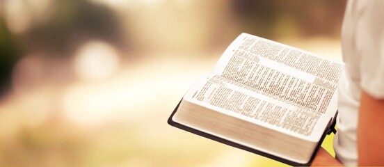 Christian holds bible book in hands with beautiful sunset.