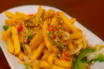 spicy french fries with chilli, garlic, bell pepper, and anchovy toppings, served on white long plate on wooden table surface
