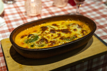 Traditional lasagna with bolognese sauce served in a rustic dish, on a table with a checkered tablecloth.