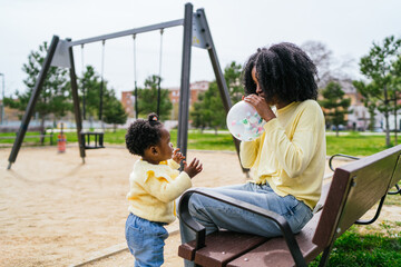 A woman and a child are sitting on a bench in a park with a balloon
