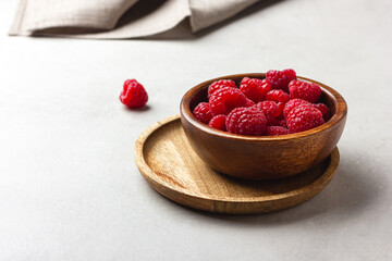 Fresh raspberries in a wooden bowl on a light grey background