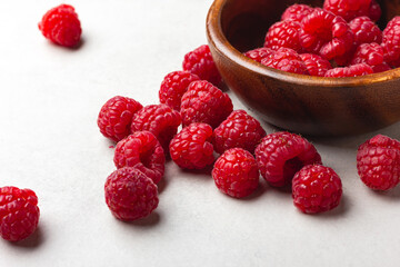 Fresh raspberries in a wooden bowl on a light grey background