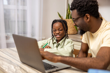 Black man with his daughter using laptop together while doing homework