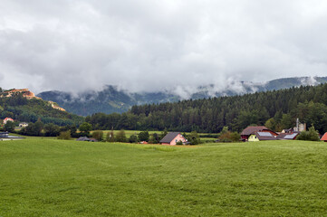 Obraz premium Beautiful mesmerizing view of a village with houses and chalets in pastures in Slovak Carpathians ridge on a foggy day. Nature background. Landscape scenery. Tourism and travel destinations concept