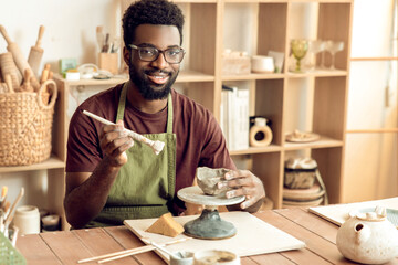 Dark-skinned bearded painting pottery and looking contented