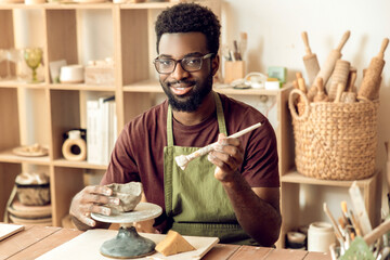 Dark-skinned bearded painting pottery and looking contented