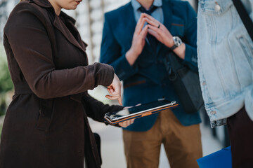 Group of professionals gathered outdoors, discussing and working on tablets and smart phones during an informal business meeting in the city.