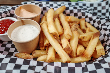 A close-up shot of a serving of golden, crispy French fries presented on a checkered paper....