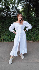 beautiful slender woman with dark hair in a white long dress posing on a city street in summer