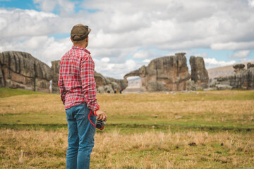 A man in a red shirt and jeans is taking a picture of a large rock formation. Huayllay Stone Forest, Peru.