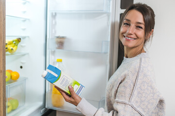 Young dark-haired woman opening fridge and taking a bottle of milk