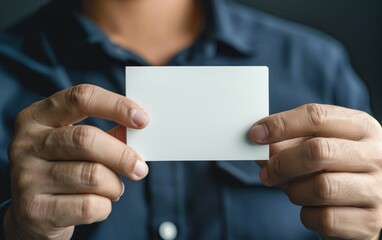 Fototapeta premium Person in a dark shirt holding a blank white card. Close-up photography with focus on the card with both hands. Business and personal identity concept for design and print.