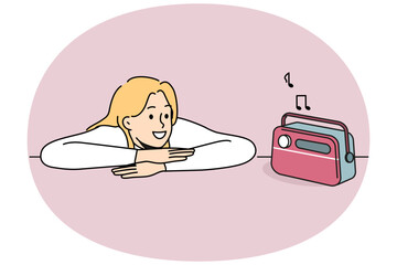 Woman is listening to radio using vintage fm receiver and enjoying analog sound of music. Hipster girl put head on table and looks with smile at retro radio device for playing compositions