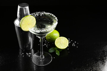 Metal shaker, delicious cocktail, limes and mint on black mirror surface, space for text