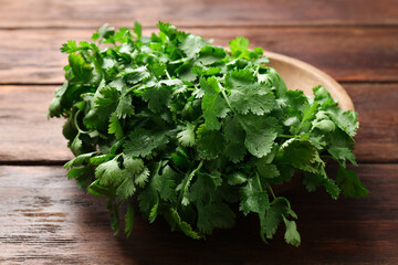 Fresh coriander in bowl on wooden table, closeup