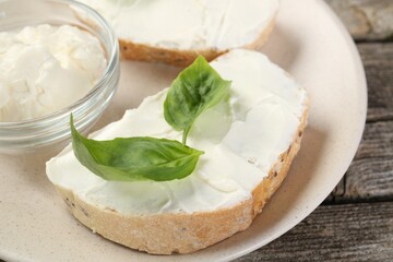 Delicious sandwiches with cream cheese and basil leaves on wooden table, closeup