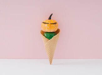 Little pumpkin with make up in ice cream cone on pastel pink and white background. Minimal autumn and summer season concept background. Funny ice cream with pumpkins idea.