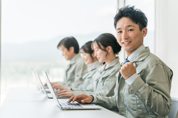 デスクワークする作業着・作業服姿の男女ビジネスマン・エンジニア（ガッツポーズ・やる気・やりがい）
