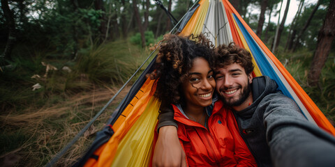 "A multiracial couple taking a selfie on a hammock at their camping site. Concept of travel, adventure, outdoors, and camping.