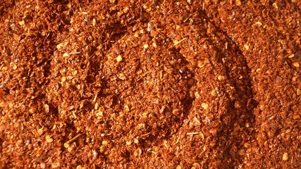 In this close-up, ground chili flakes dazzle with their fiery red and orange hues. The coarse texture, adorned with visible seeds and dried chili fragments, hints at a potent, flavorful kick.
