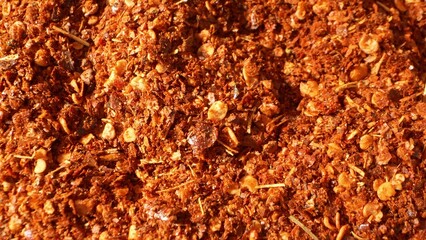Close-up of ground chili: a fiery tapestry of crushed flakes and seeds, their coarse texture a testament to their potency. Rich red and orange hues dance, promising a burst of flavor and heat.
