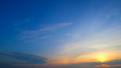 A serene sunrise with a gradient sky transitioning from deep blue at the top to soft orange near the horizon. Wispy clouds are lightly scattered, enhancing the tranquil morning atmosphere.
